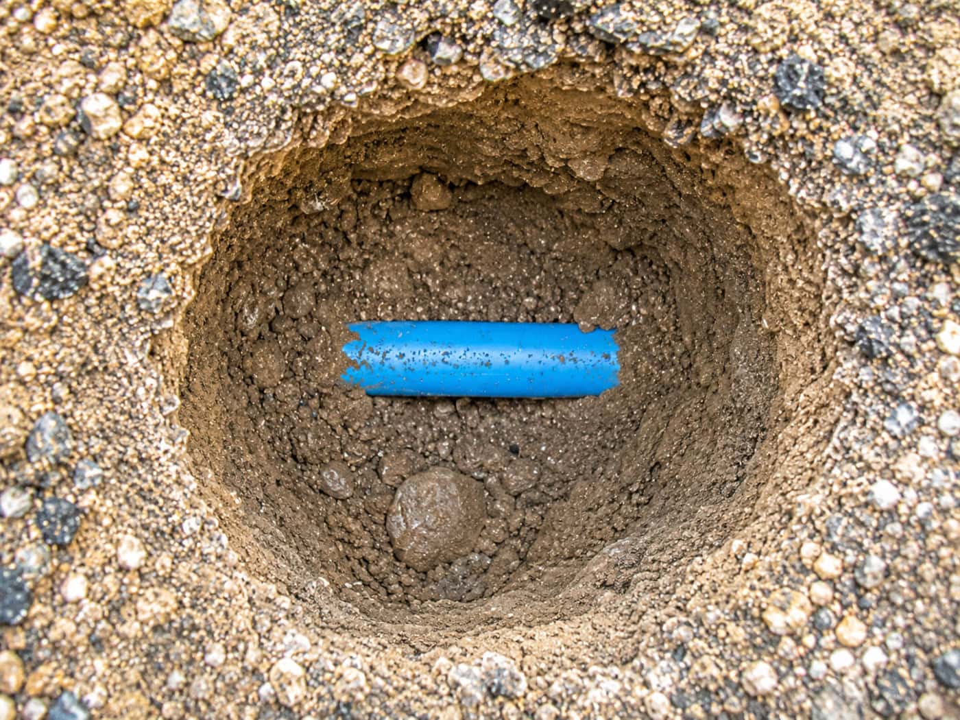 Excavated blue MDPE mains water supply pipe during underground leak detection investigation.